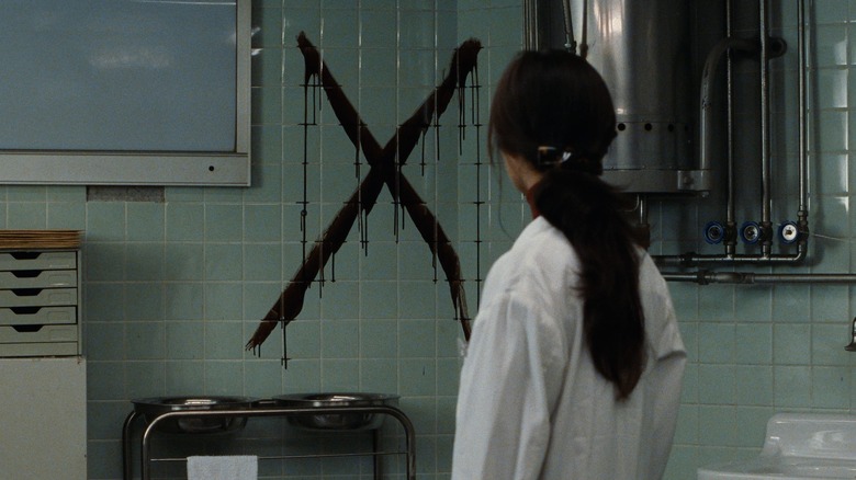 A shot from Cure, in which a woman looks on at an "X" sprawled on a wall.