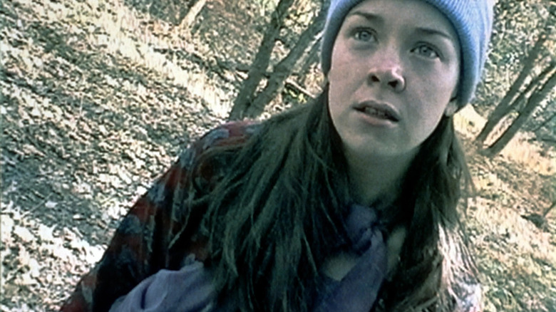 Heather Donahue as herself in The Blair Witch Project, standing in the woods and looking at someone holding the camera.