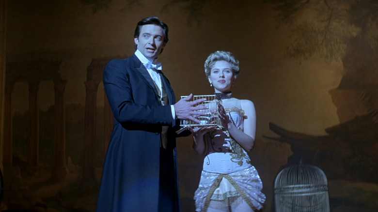 Hugh Jackman as Robert Angier and Scarlett Johansson as Olivia Wenscombe in The Prestige, standing on stage looking out at the audience, each holding the same cage containing a dove.