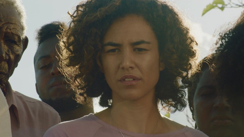 Bárbara Colen as Teresa in Bacurau, surrounded by fellow visitors as they stand outside looking down at something.