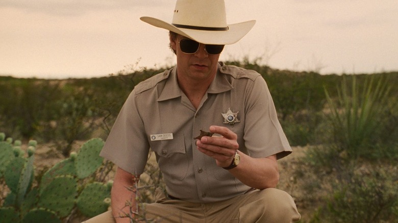 Chris Cooper as Sheriff Sam Deeds in Lone Star, in his sheriff gear out in the Texas desert, crouched down and looking at a sheriff badge.
