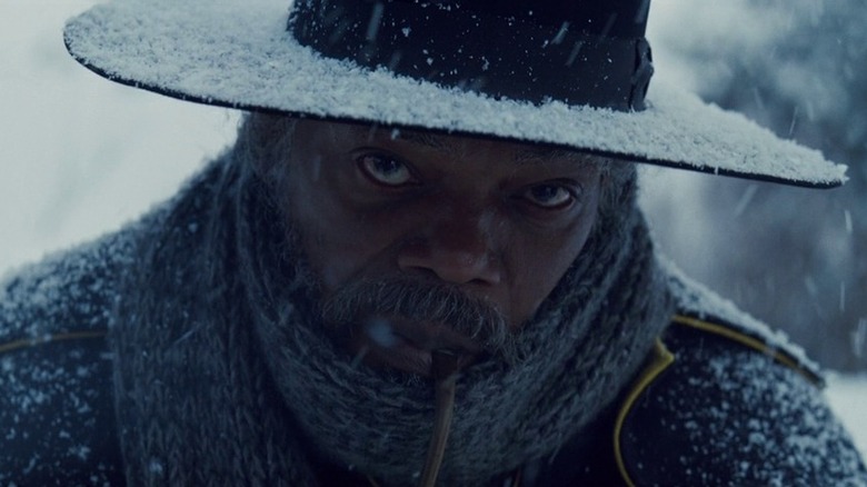 A close-up of Samuel L. Jackson as Major Marquis Warren in The Hateful Eight, wrapped up in a scarf with his large-brimmed hat on and a pipe in his mouth, head slightly down as the snow bears down.