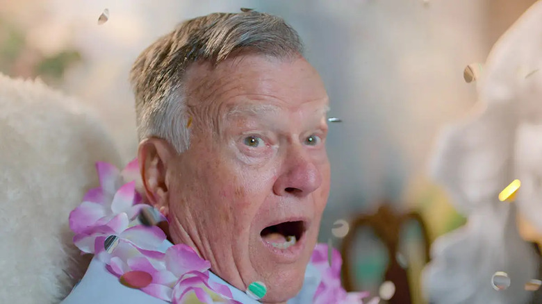 Dick Johnson wearing lei looking surprised with confetti around him in Dick Johnson Is Dead