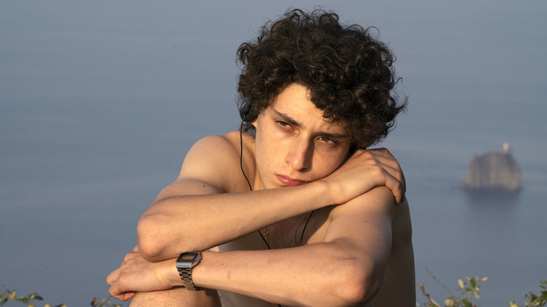 Filippo Scotti as Fabietto sitting in front of ocean with headphones in looking bored in The Hand of God