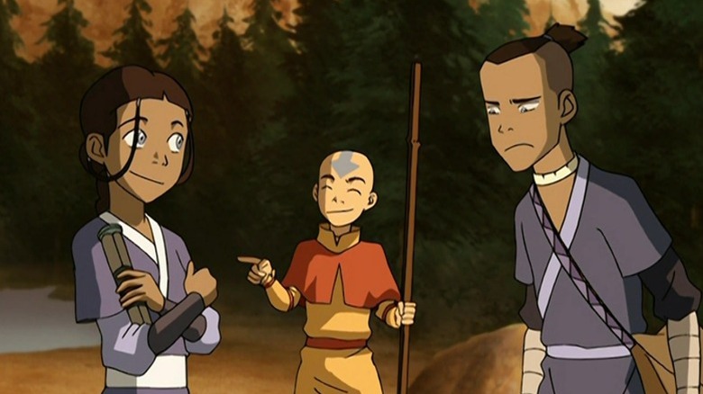 Aang pointing and smiling with his eyes closed at a proud Katara while Sokka glares on Avatar: The Last Airbender