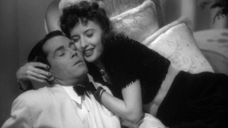 Barbara Stanwyck as Jean Harrington lying on a sofa and embracing Henry Fonda as Charles Pike as he slips towards the floor in The Lady Eve
