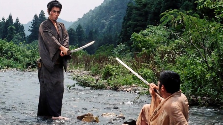 Rōnin (Tatsuya Nakadai) stands with his sword in a creek over Zatoichi (Shintarō Katsu) in Zatoichi Goes to the Fire Festival