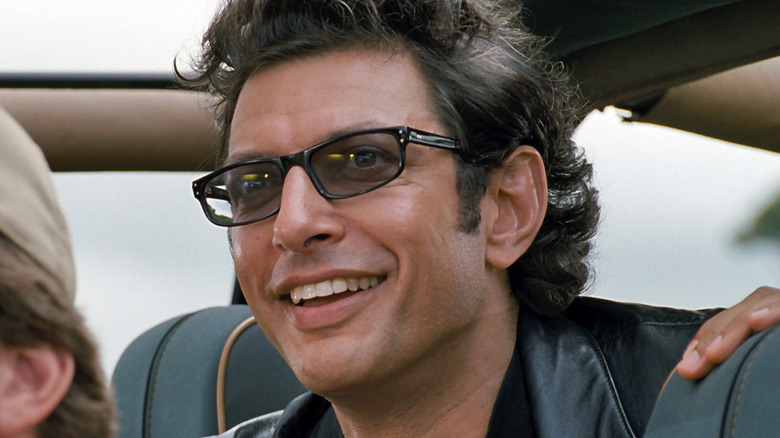 Jeff Goldblum as Ian Malcolm, smiling in a car in Jurassic Park.