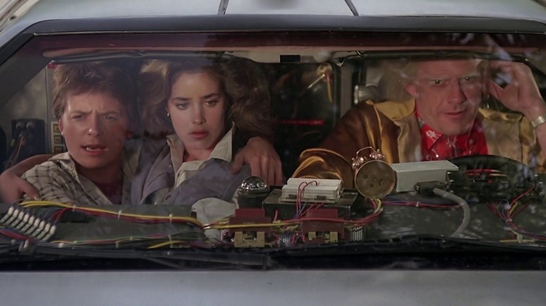 Marty McFly (Michael J. Fox), Jennifer Parker (Claudia Wells), and Doc Brown (Christopher Lloyd) crowd into a DeLorean in Back to the Future