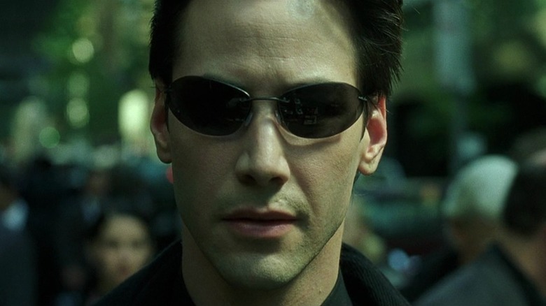 Neo (Keanu Reeves) walks down a street wearing sunglasses in The Matrix
