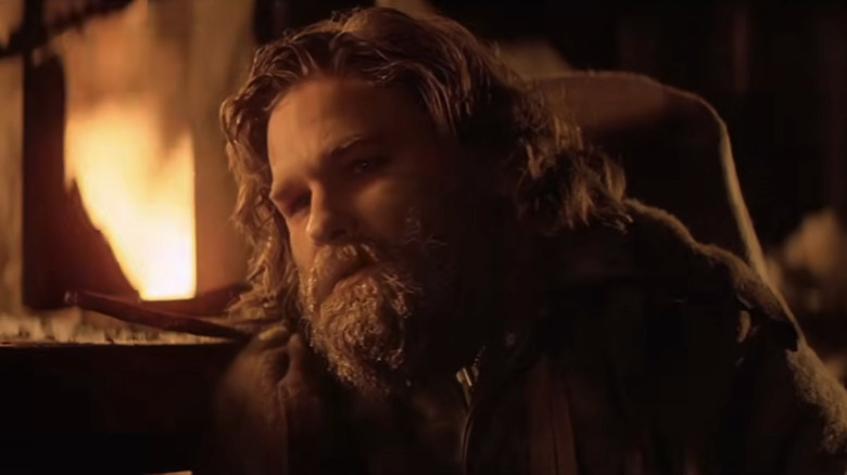 An exhausted RJ McCready (Kurt Russell) leans towards a fire in The Thing (1982)