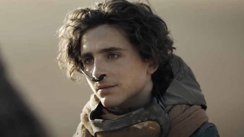 Timothée Chalamet as Paul Atreides in Dune: Part One, wearing his water retaining device and standing outside.