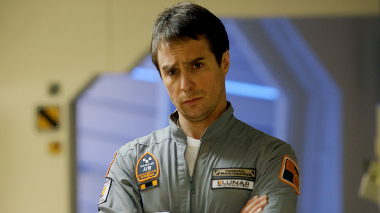Sam Rockwell as Sam Bell, crossing his arms in confusion in Moon.