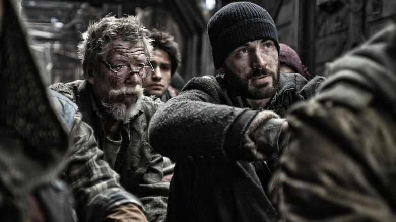John Hurt as Gilliam and Chris Evans as Curtis Everett, sitting together on the ground in Snowpiercer.