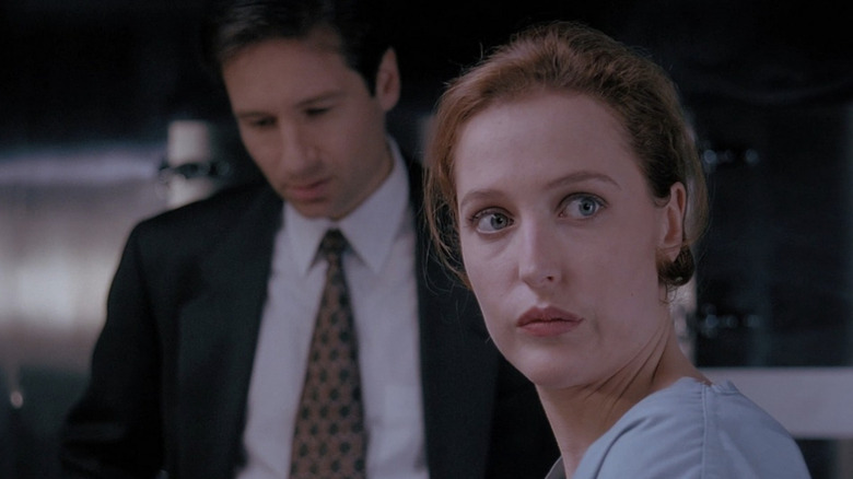 Dana Scully (Gillian Anderson) looks to her left while Fox Mulder (David Duchovny) stares down in the background in The X-Files
