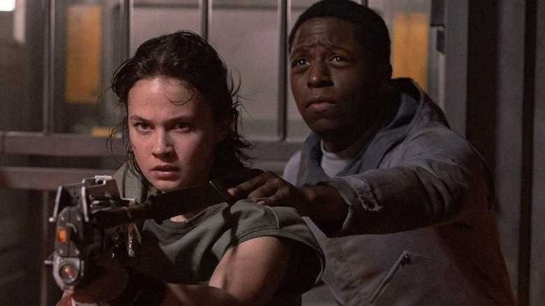 David Jonsson as Andy the andriod holding on to Cailee Spaeny as Marie Raines "Rain" Carradine as she wields a gun in Alien: Romulus