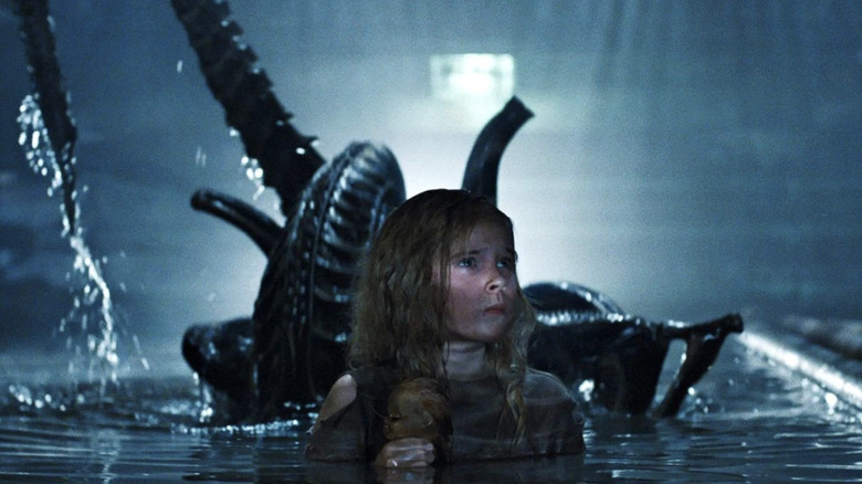 Carrie Henn as Rebecca "Newt" Jorden holding a doll in the water in front of a xenomorph Aliens