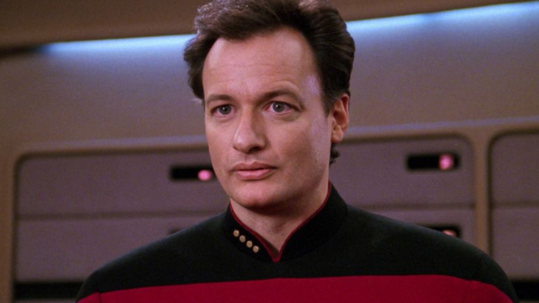 Q (John de Lancie) stands wearing a Starfleet uniform in Star Trek: The Next Generation
