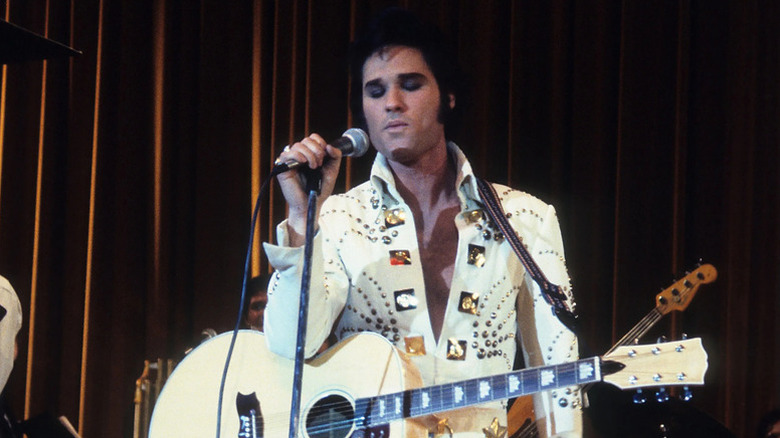 Elvis Presley (Kurt Russell) closes his eyes as he sings into a microphone on stage in Elvis (1979)