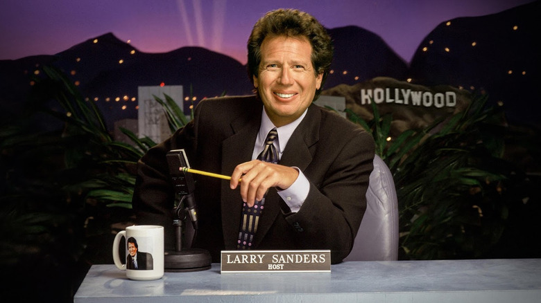Garry Shandling as Larry Sanders sitting at this talk show desk on The Larry Sanders Show