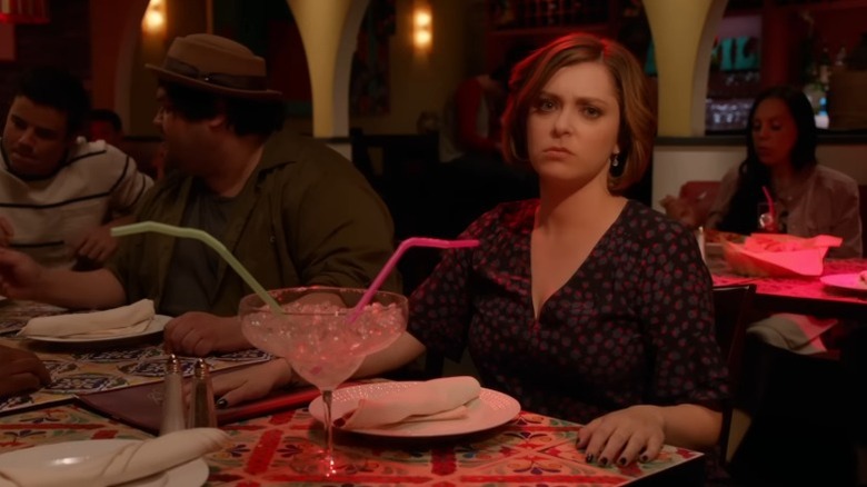 Rachel Bloom as Rebecca Bunch sitting at a restaurant table and looking sternly at the camera under colorful lighting on Crazy Ex-Girlfriend