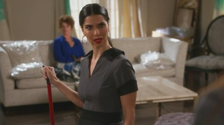Roselyn Sanchez as Carmen Luna standing in the living room and holding a broom on Devious Maids