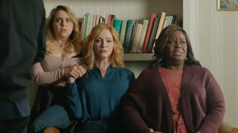 Mae Whitman as Annie Marks, Christina Hendricks as Beth Boland, and Retta as Ruby Hill sitting together and holding hands with fearful expressions as a man passes by them on Good Girls