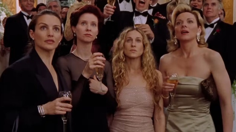 Kristin Davis as Charlotte York, Cynthia Nixon as Miranda Hobbes, Sarah Jessica Parker as Carrie Bradshaw, and Kim Cattrall as Samantha Jones standing together at a wedding and looking up on Sex and the City
