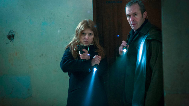 Clémence Poésy as Elise Wassermann and Stephen Dillane as Karl Roebuck holding pointing flashlights and a gun as they walk into a room in The Tunnel