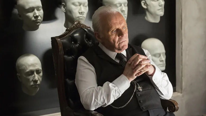 Anthony Hopkins as Dr. Robert Ford sitting at a desk with android face molds behind him in Westworld