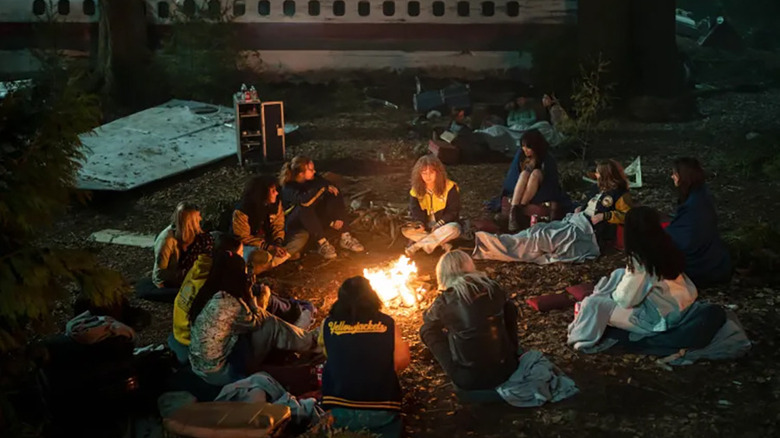 The Yellowjackets team sitting around a fire next to their crashed plane in Yellowjackets