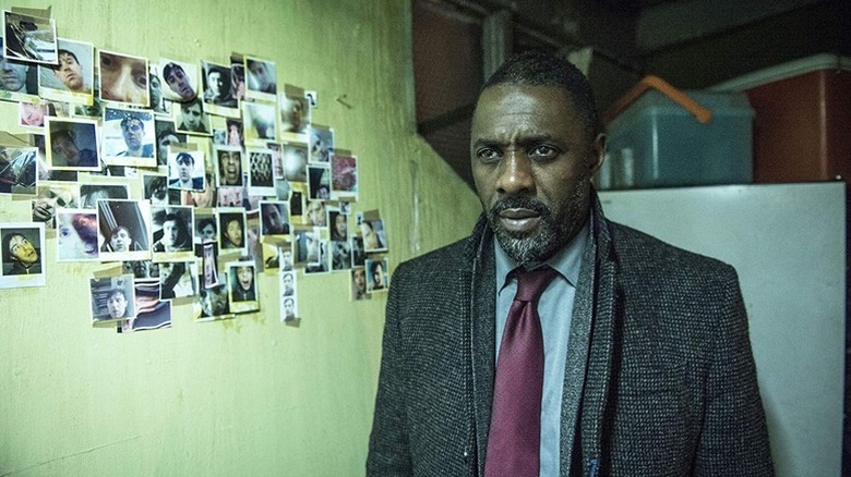 John Luther (Idris Elba) stands by a wall of polaroid photographs in Luther