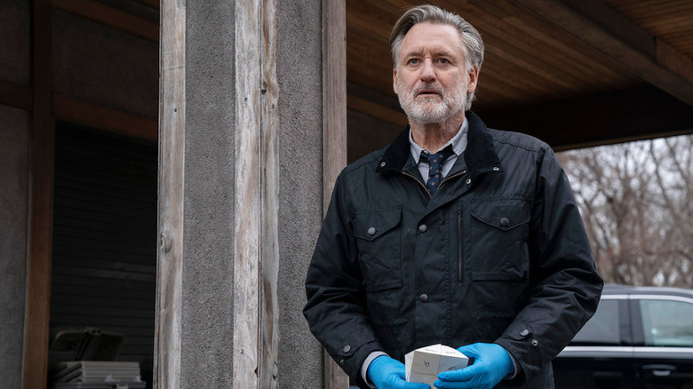 Harry Ambrose (Bill Pullman) holds a paper puzzle by a wooden beam in The Sinner