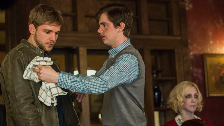 A bloodied Norman Bates (Freddie Highmore) presses a towel against Dylan Massett (Max Thieriot) with a body in the background in Bates Motel