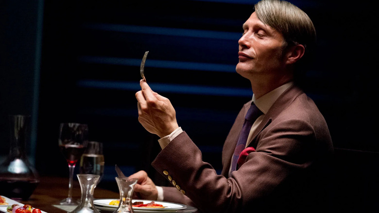 Hannibal Lecter (Mads Mikkelsen) smiles approvingly at a fork on Hannibal