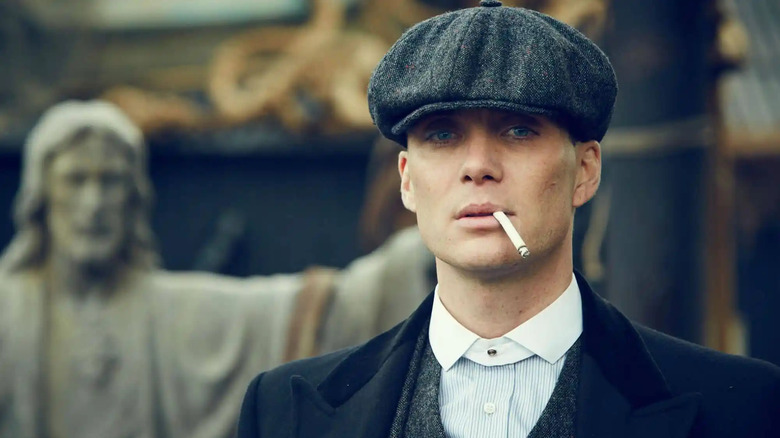 Tommy Shelby (Cillian Murphy) stands with a cigarette in his mouth by a Jesus statue in Peaky Blinders