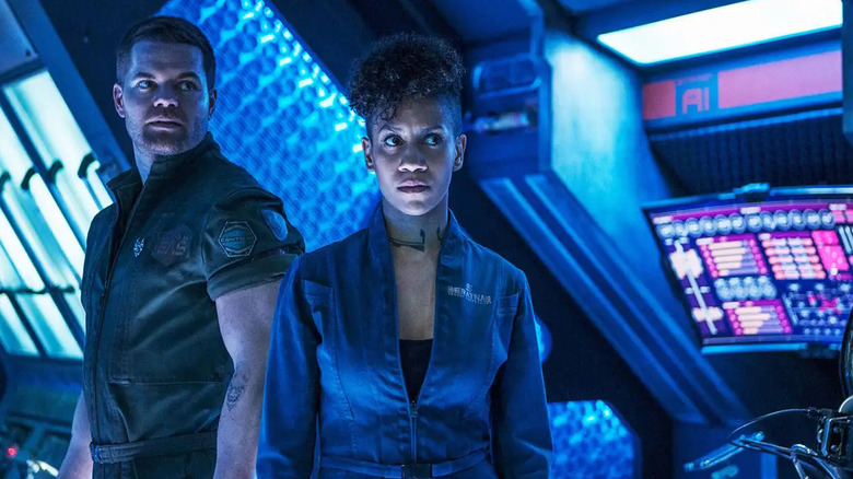 Amos Burton (Wes Chatham) and Naomi Nagata (Dominique Tipper) stand next to ship consoles in The Expanse