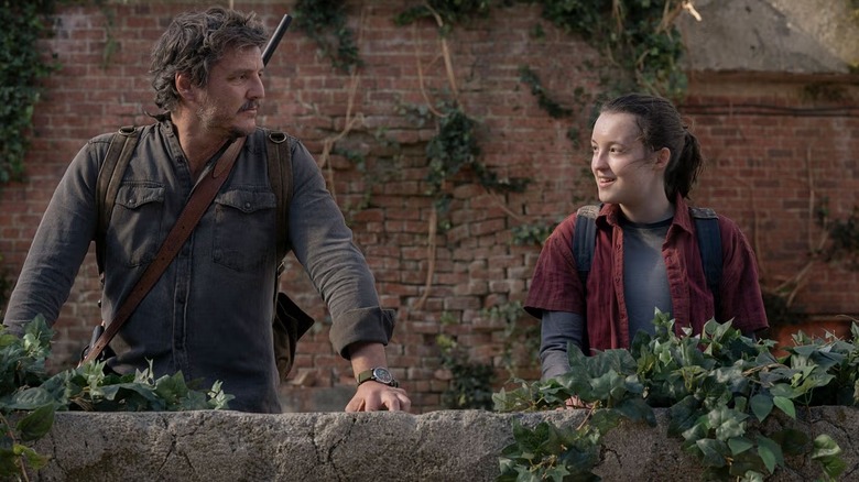 Joel Miller (Pedro Pascal) and Ellie (Bella Ramsey) stand on an overgrown terrace in The Last of Us