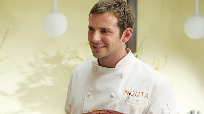 Bradley Cooper as Jack, holding a fish in the dining room in Kitchen Confidential