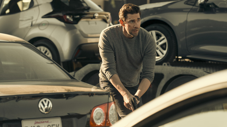 Jack Ryan (John Krasinski) holding a gun amid cars on Tom Clancy's Jack Ryan