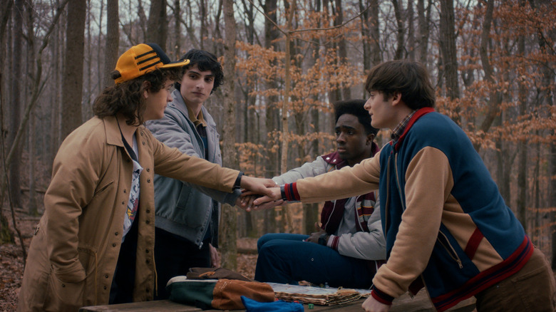 Gaten Matarazzo's Dustin Henderson, Finn Wolfhard's Mike Wheeler, Caleb McLaughlin's Lucas Sinclair, and Noah Schnapp's Will Byers putting their hands in the middle in Stranger Things
