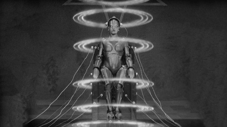 A shot of the Maschinenmensch in Metropolis, a robot being sat in a chair attached to electrical wiring and encircled by energy rings.