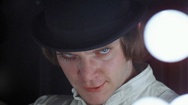 A close-up of Malcolm McDowell as Alex DeLarge in A Clockwork Orange, looking menacingly upward as he tilts his head down, wearing his iconic black bowler hat.