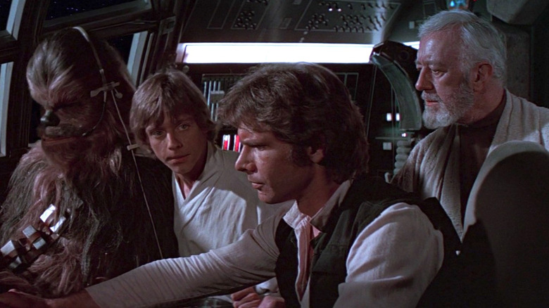 Mark Hamill as Luke Skywalker, Harrison Ford as Han Solo, Alec Guinness as Obi-Wan "Ben" Kenobi, and Peter Mayhew as Chewbacca in Star Wars, gathered around the cockpit console of the Millennium Falcon.