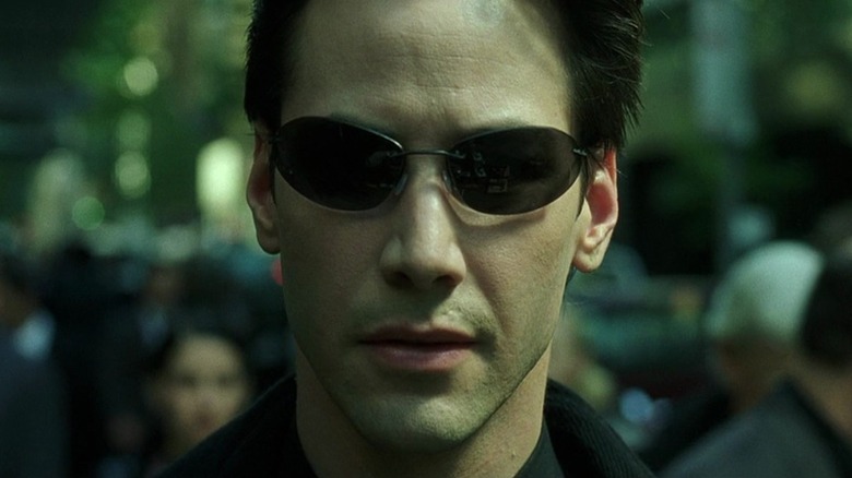 A close-up of Keanu Reeves as Neo in The Matrix, wearing his wireframe oblong sunglasses.