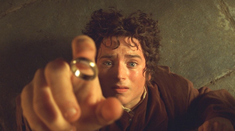 Elijah Wood as Frodo Baggins in The Lord of the Rings: The Fellowship of the Ring, looking directly up toward the camera as he lays on his back on the floor, lifting his hand and letting the One Ring fall onto his finger.