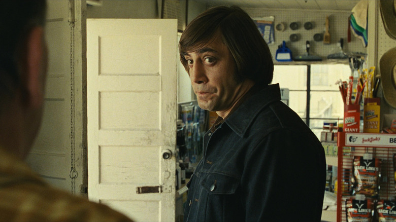 Javier Bardem as Anton Chigurh in No Country For Old Men, standing in a convenient store and giving a slightly absurd and inquisitive look with wide eyes to the person he's talking to.