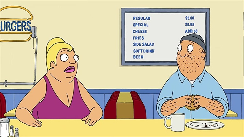 A woman sits at the bar of the burger place, looking at a man in the middle of eating