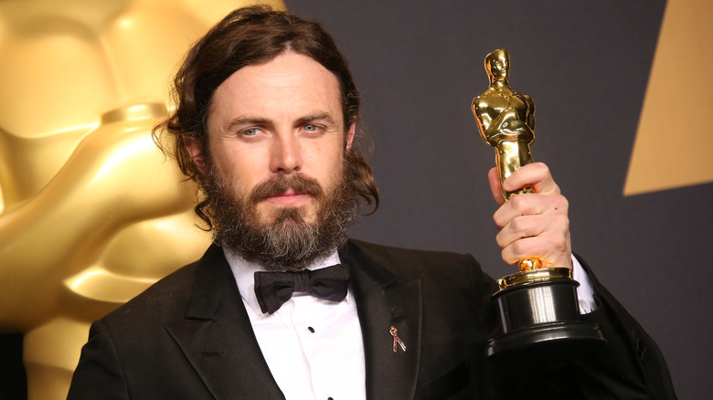 Casey Affleck in tux with beard holding up Oscar in 2017
