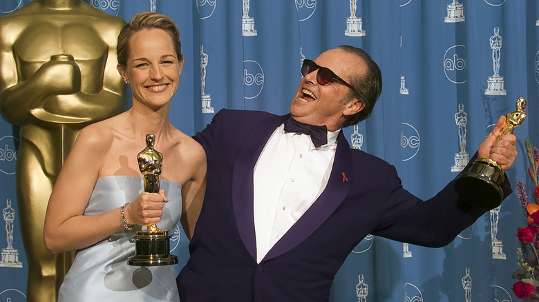 Helen Hunt in blue dress smiling and holding Oscar next to Jack Nicholson in purple suit leaning over with mouth open and Oscar in hand in 1998